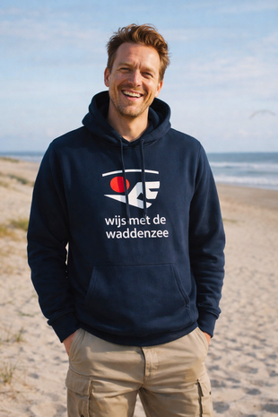 Thomas aan zee met navyblauwe hoodie met rood‑wit Waddenzee‑logo en de tekst &lsquo;wijs met de waddenzee